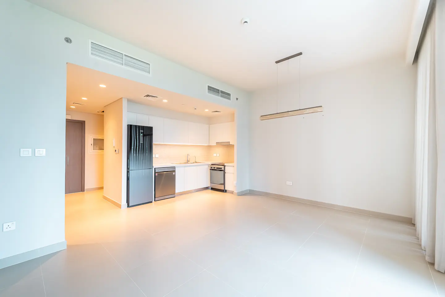 Bright, modern apartment with white walls, tile floors, and an open kitchen featuring stainless steel appliances.