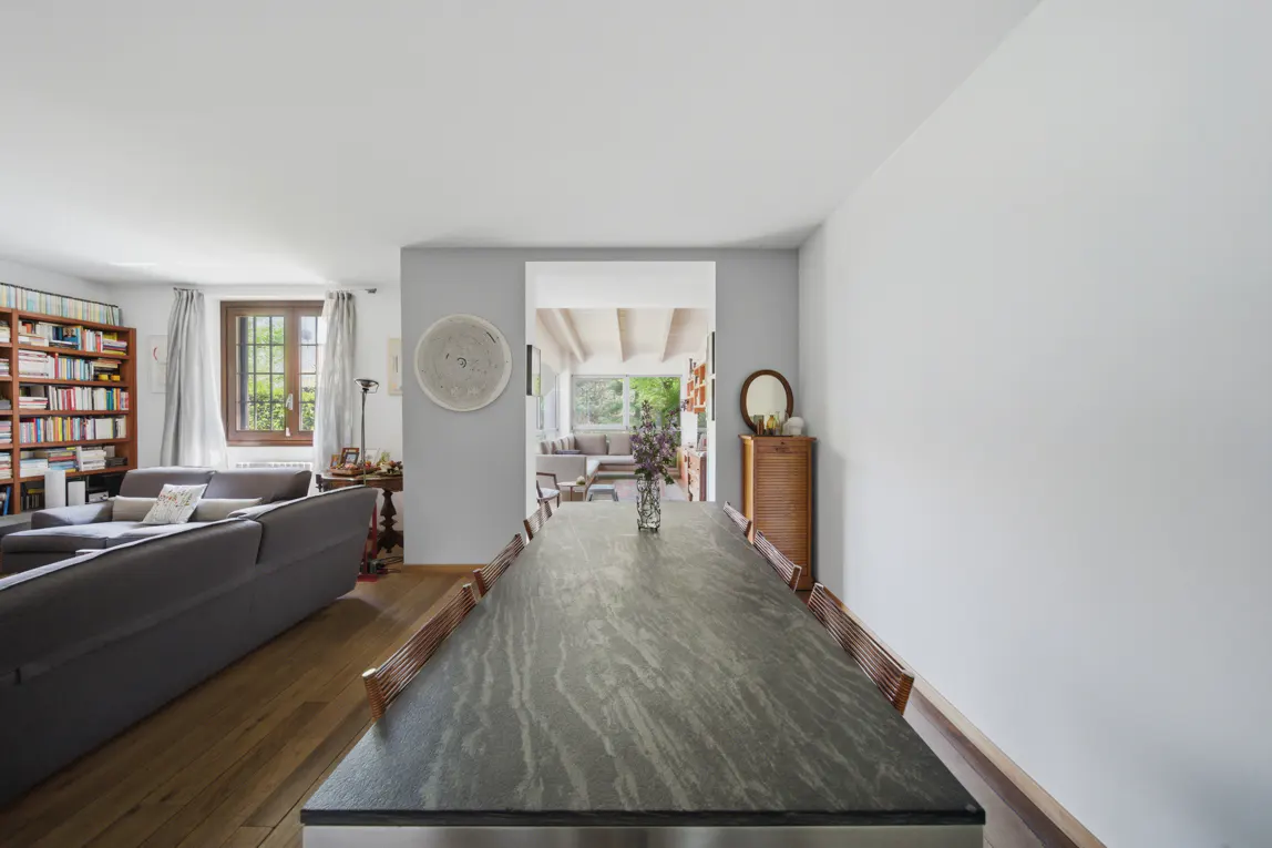 A bright, open-concept home interior with a long, dark gray dining table and a gray sofa in the background.