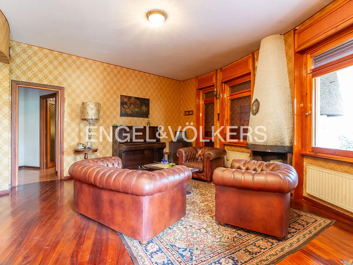 Living room with brown leather sofas, piano, and fireplace. The walls are patterned wallpaper, and the floor is hardwood with a rug.