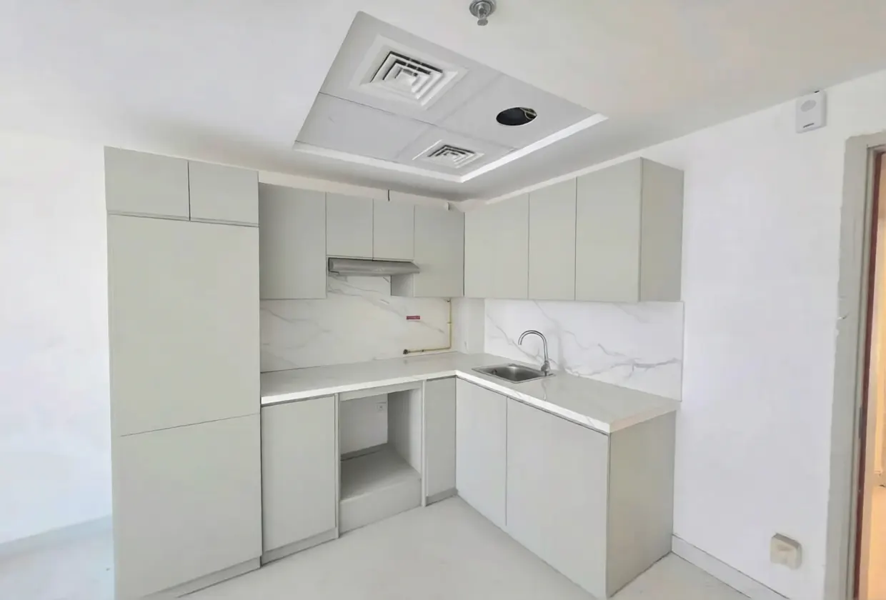 A bright, empty kitchen with gray cabinets, white marble backsplash, and a stainless steel sink.