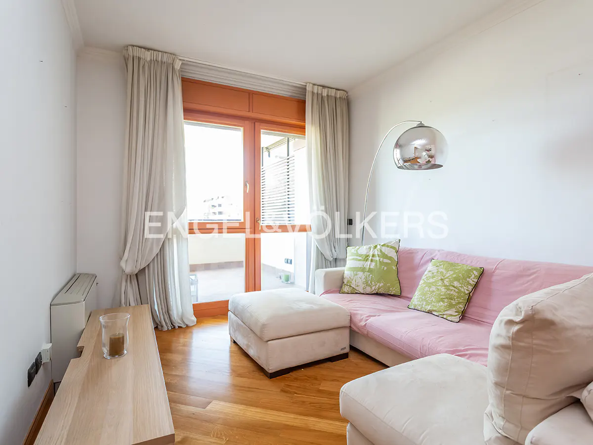 Living room with wood floors, white walls, and a pink sofa with green pillows. A glass door leads to a balcony.