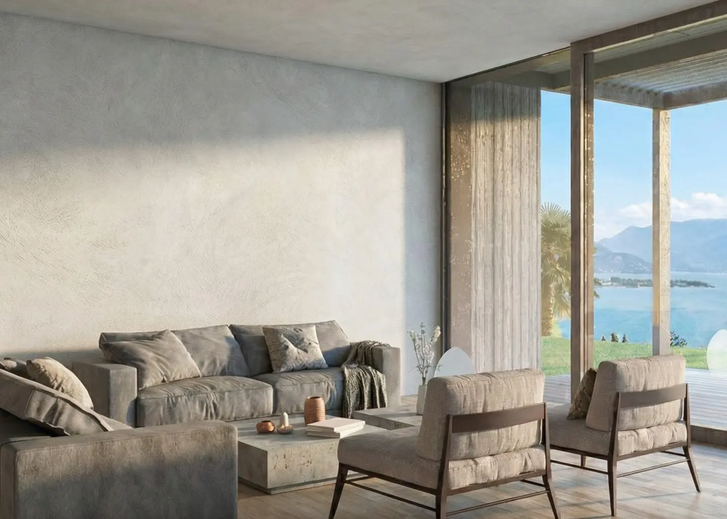 Living room with gray sofa, chairs, and concrete table. Large windows offer a view of a lake and mountains.