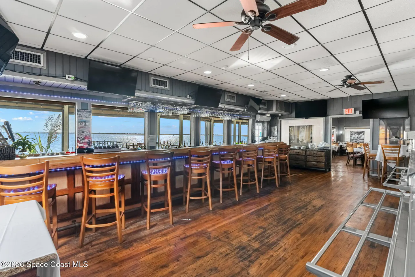 Interior view of a restaurant bar with wood floors, bar stools, and a water view.