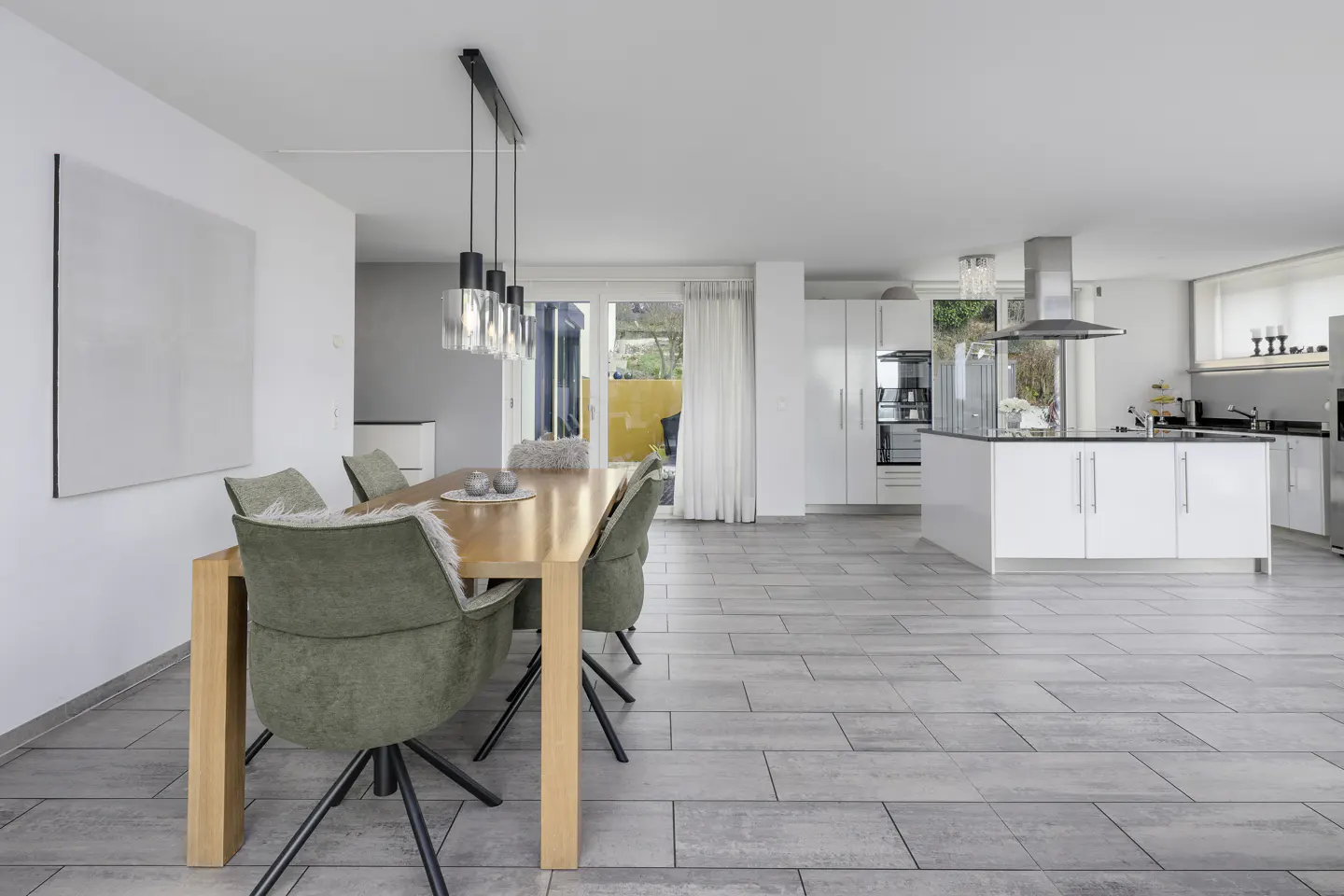 Open concept home with a wood dining table, green chairs, and a white kitchen island on gray tile flooring.