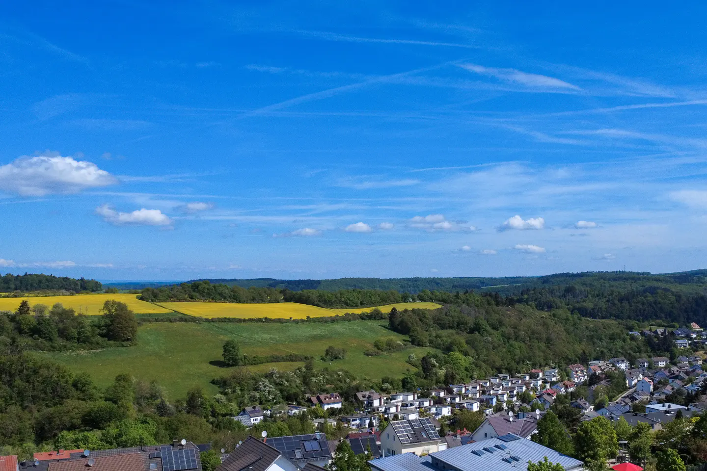 Scenic view of a town nestled among green hills and a bright yellow field under a blue sky.
