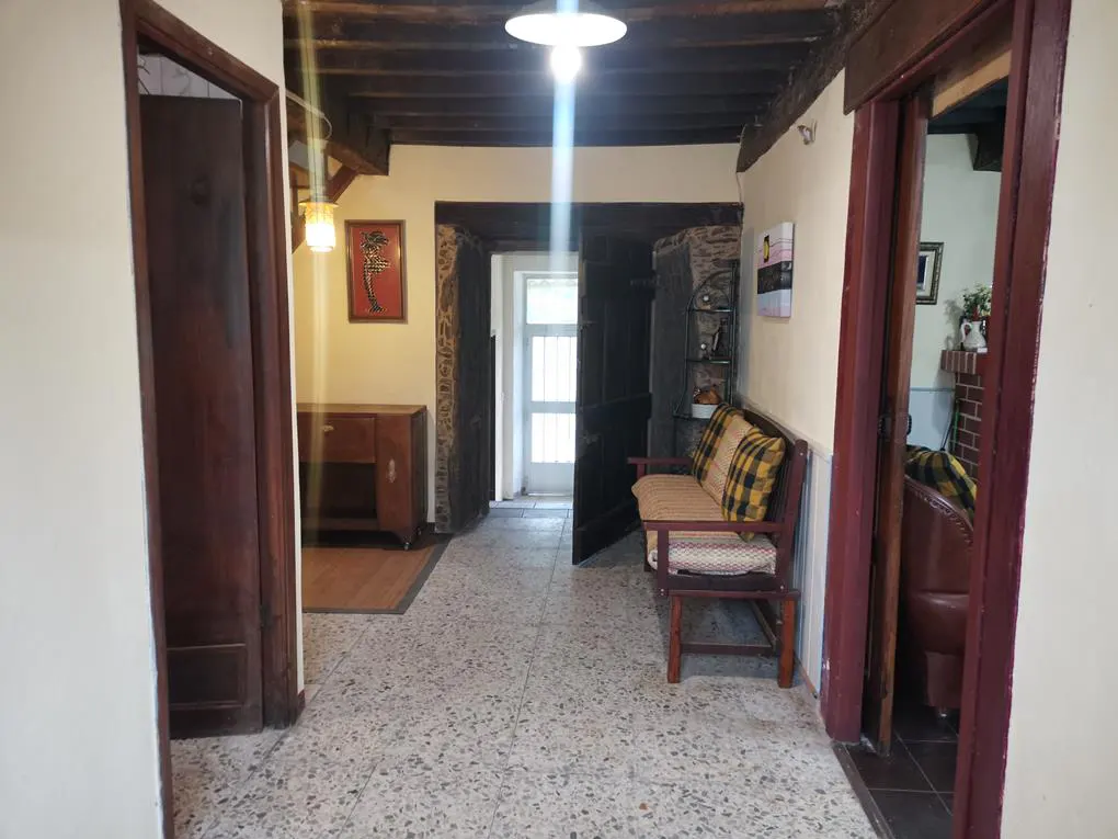Hallway with terrazzo floor, dark wood beams, and doorways. A bench with yellow plaid cushions sits near an open door.