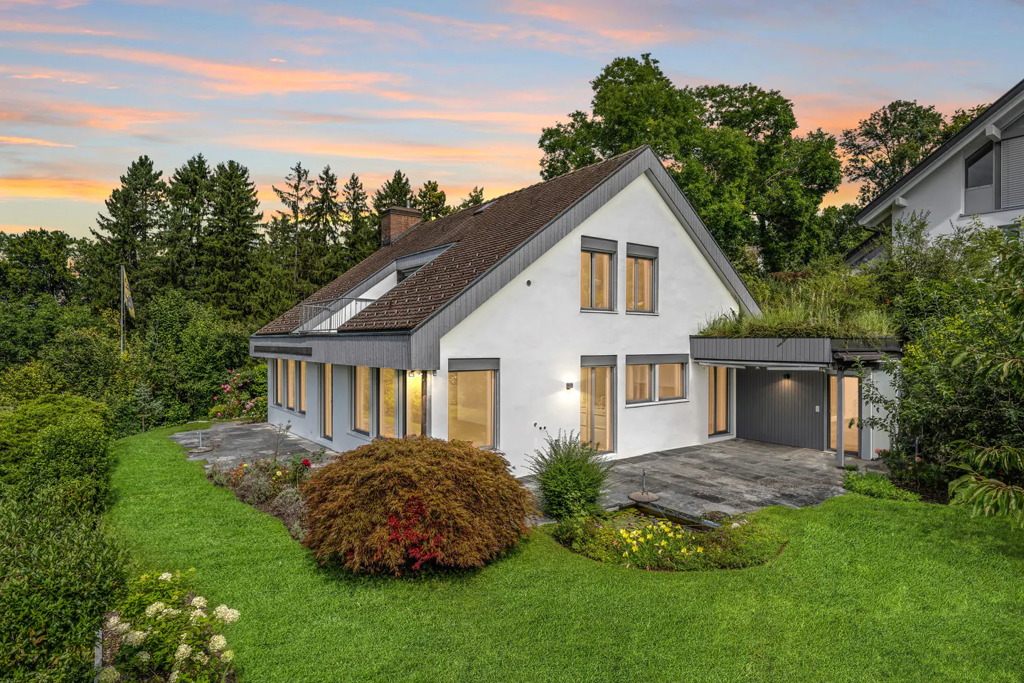 Exterior view of a white two-story house with a brown roof, green lawn, and trees at sunset.