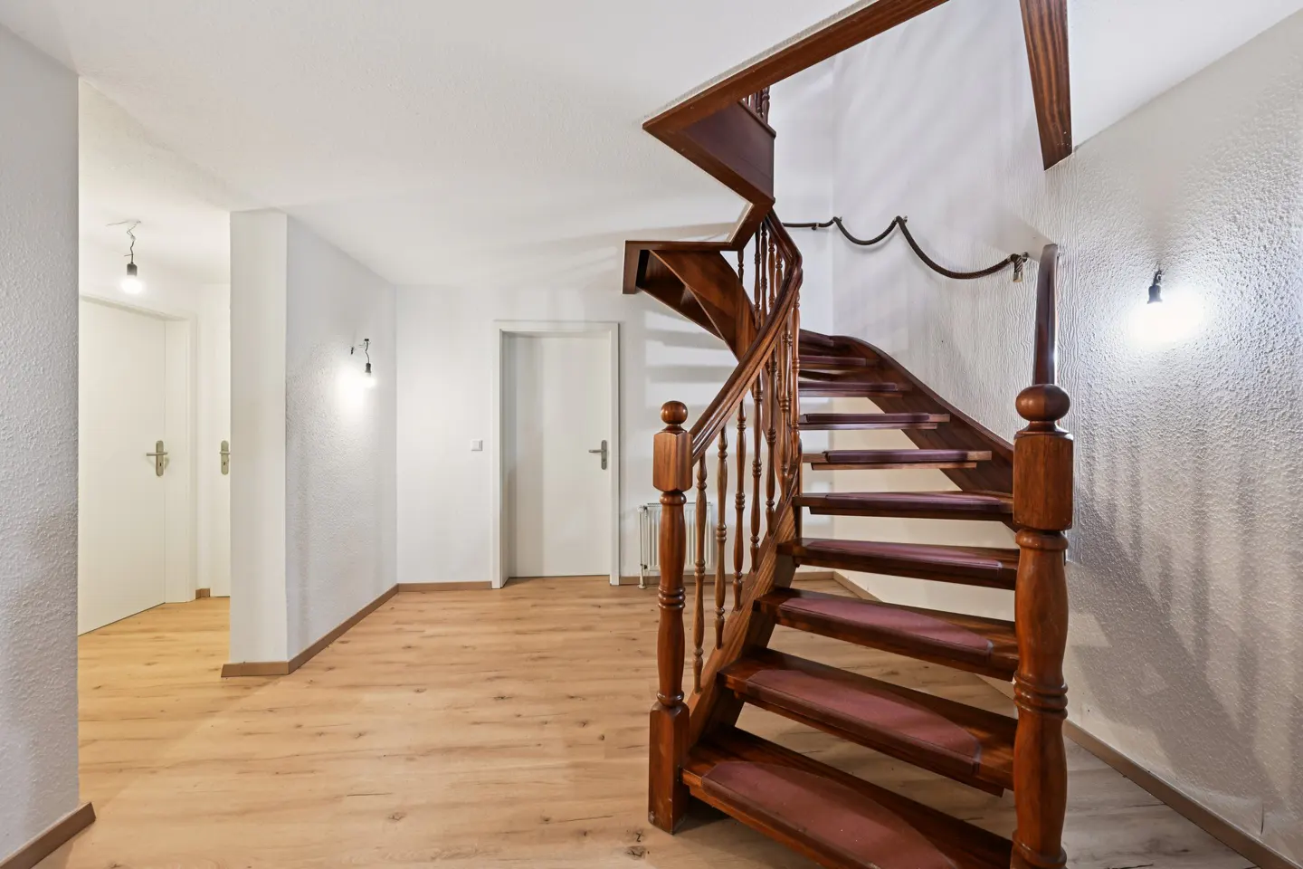 Interior view of a home featuring a wooden spiral staircase with red carpet treads, white walls, and light wood floors.