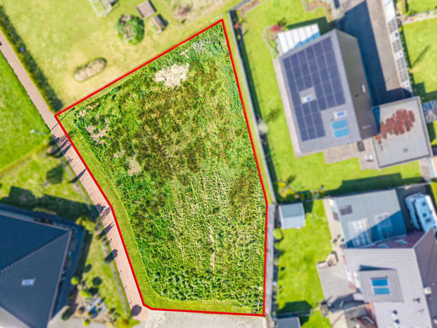 Aerial view of a vacant lot with tall grass, outlined in red, surrounded by houses and green lawns.
