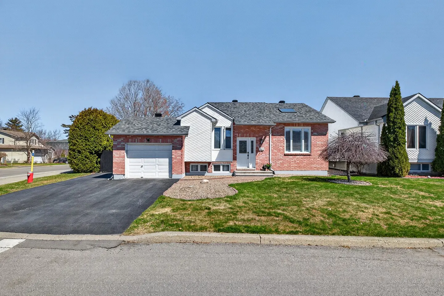 A single-story red brick house with a white garage door and a green lawn on a sunny day.