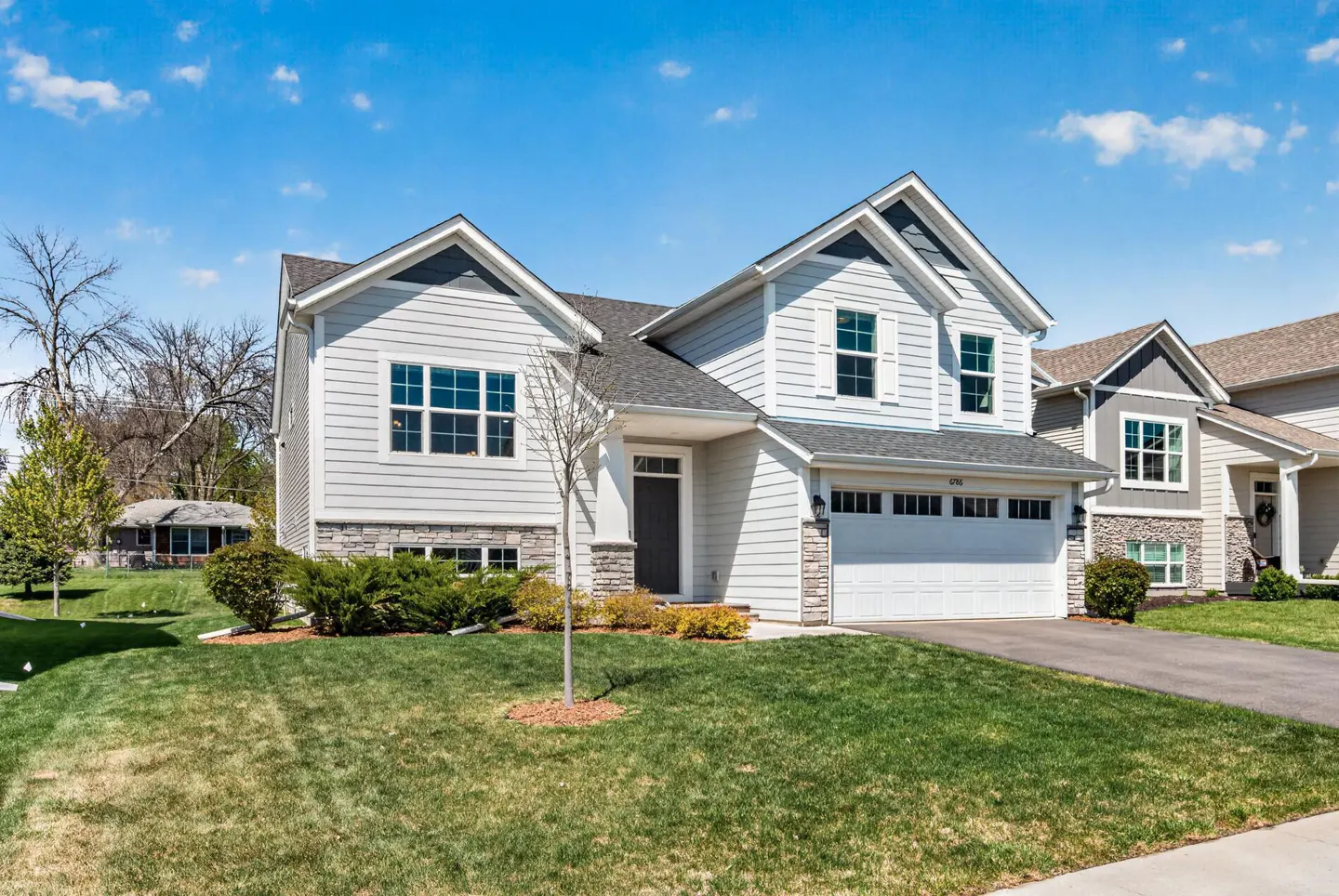 Two-story house with light gray siding, white trim, and a gray roof on a sunny day. Green lawn and driveway in front.