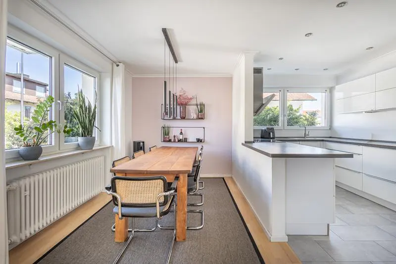 Bright, modern kitchen with a wood dining table, six chairs, and a white kitchen island. Plants sit on the windowsill.