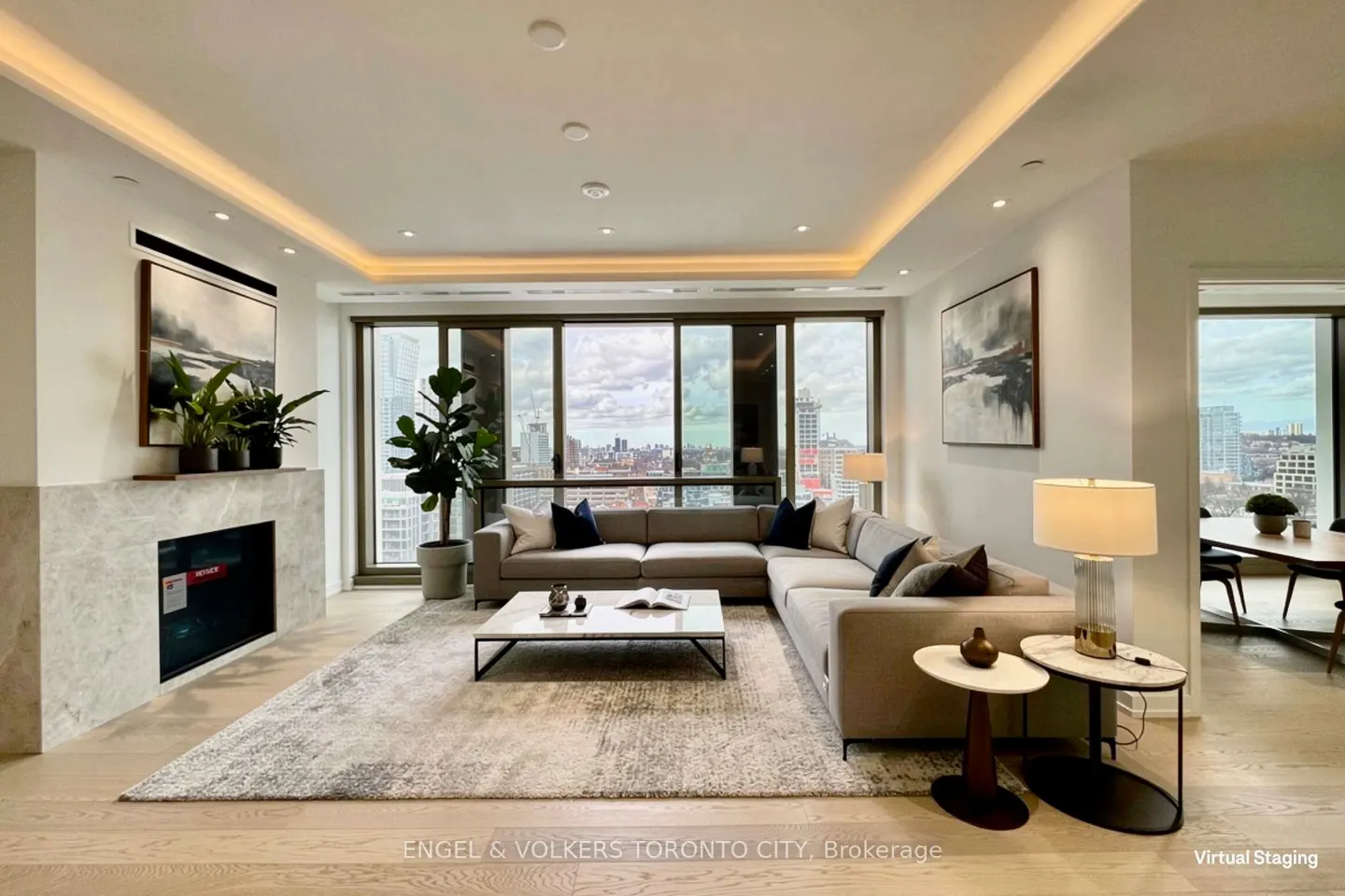 Bright living room with a gray sectional sofa, marble fireplace, and city views from large windows. Neutral tones and modern decor.