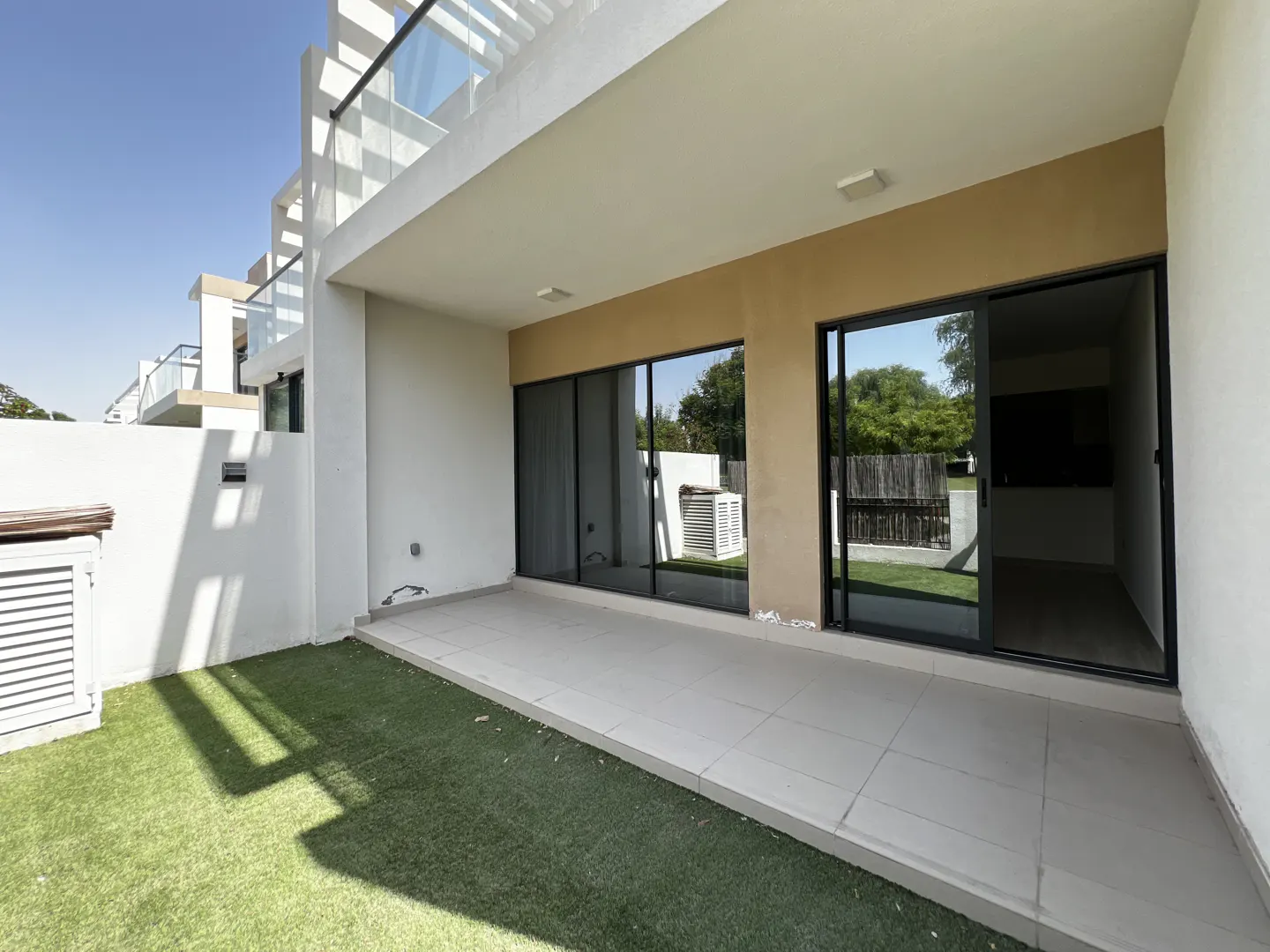 A modern townhouse patio with gray tile, artificial grass, and black sliding glass doors.