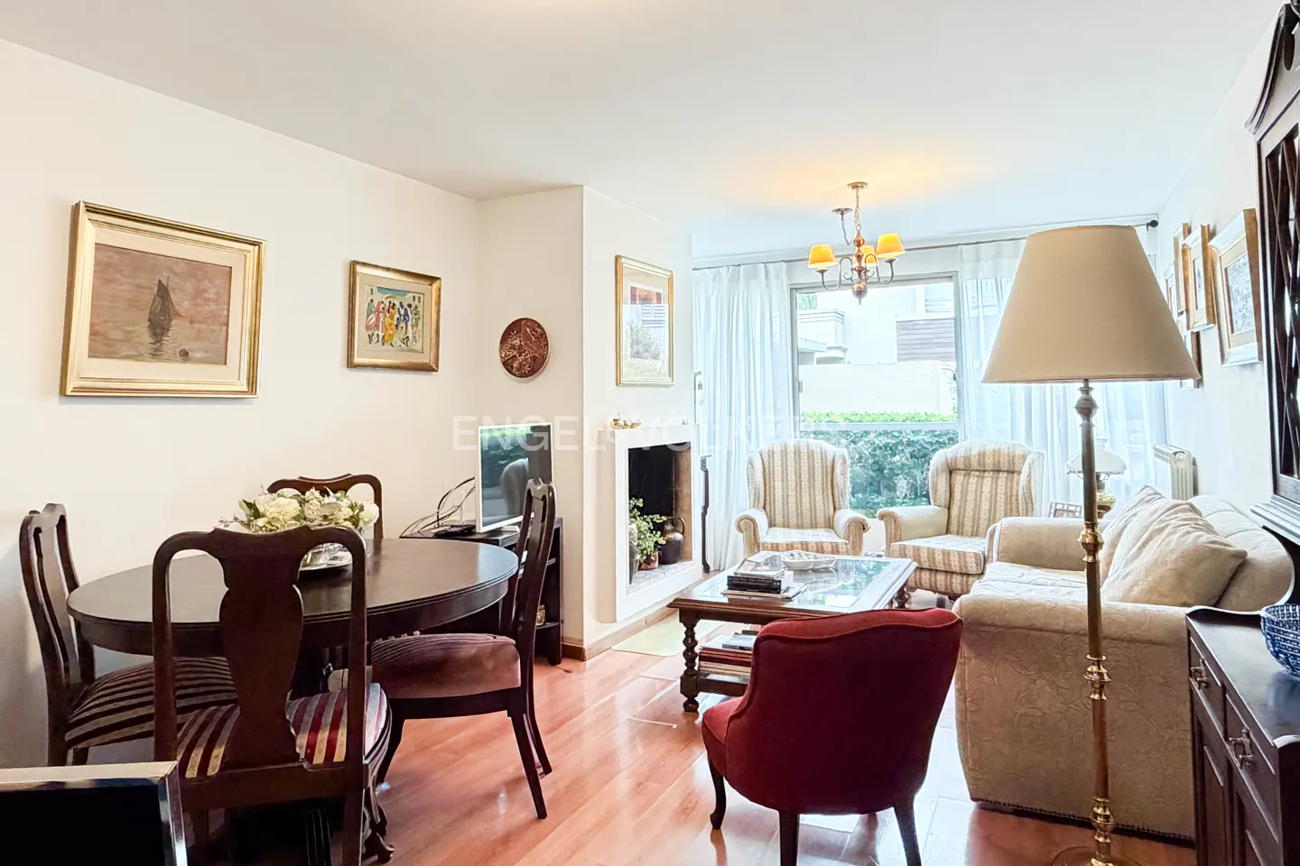 A bright living room with wood floors, a dining table, a fireplace, and a seating area with a sofa and chairs.