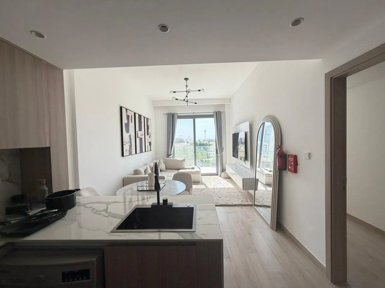 A bright, modern apartment interior with a kitchen island, living area, and balcony. Neutral tones and natural light create an open, airy feel.