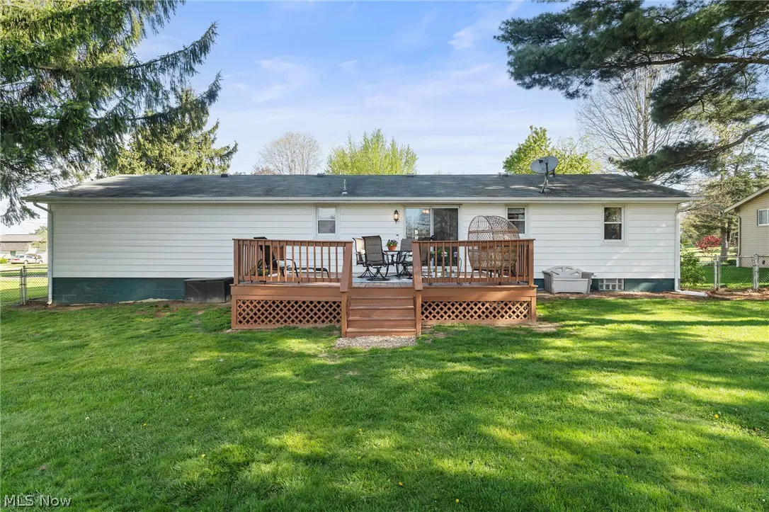 Backyard view of a white house with a wooden deck, table, chairs, and green lawn.