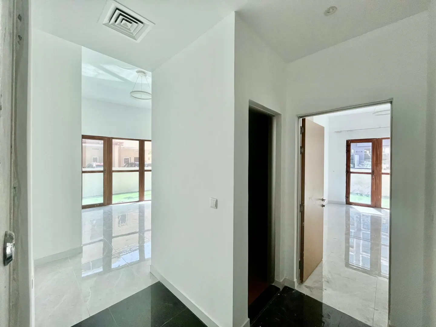 A bright, empty hallway with white walls and black and white tile floors leads to rooms with large windows.