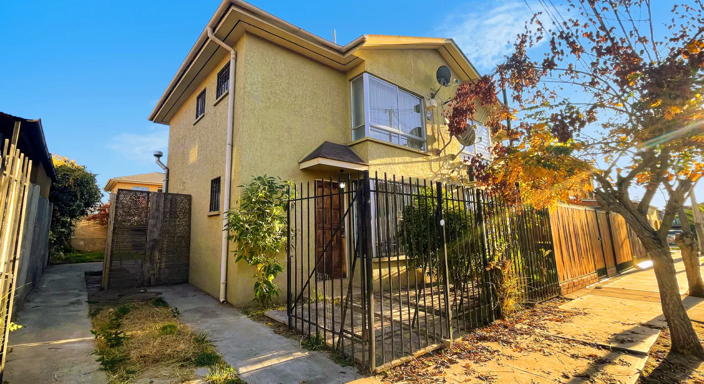 Two-story yellow house with a black iron fence and a brown door, viewed from the street.