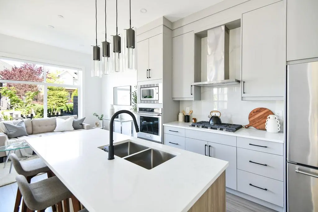 Bright, modern kitchen with gray cabinets, stainless steel appliances, and a white countertop island with a black faucet and sink.
