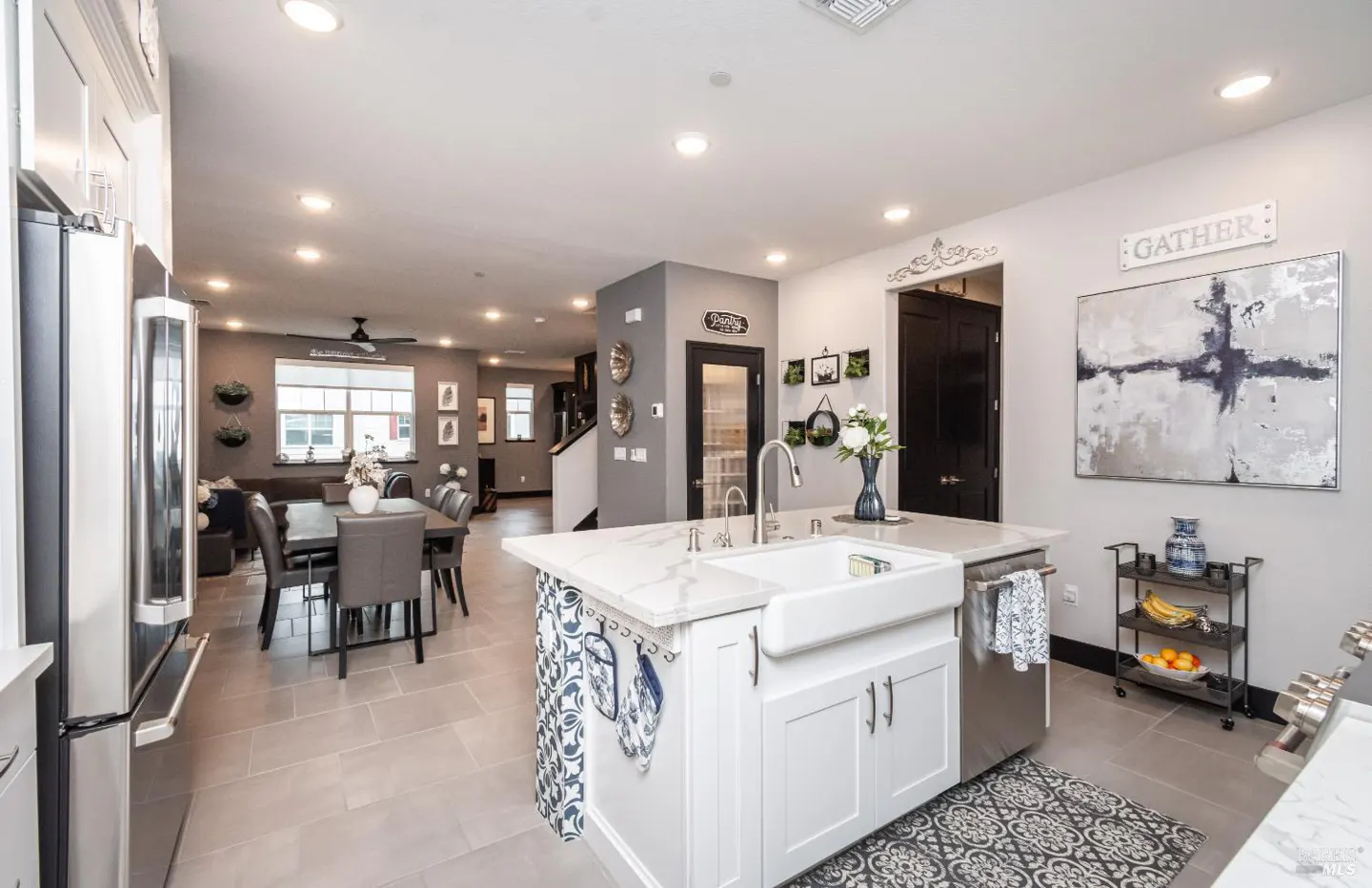 Open concept kitchen and dining area with white island, stainless steel appliances, and gray walls.