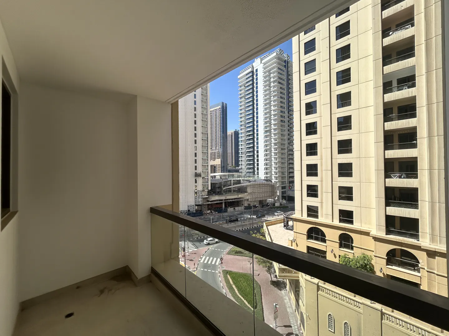 View from a modern apartment balcony overlooking a city street, tall beige and white skyscrapers, and a clear blue sky.