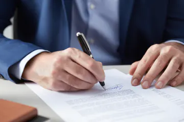 Person signing a document with a pen