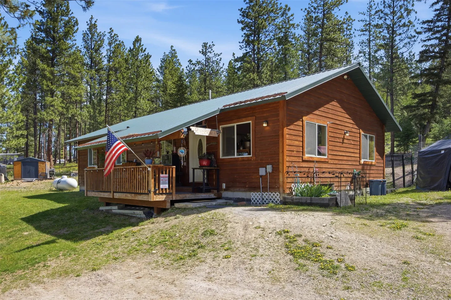Exterior view of a brown, wood-sided house with a green metal roof and a wooden porch with an American flag.