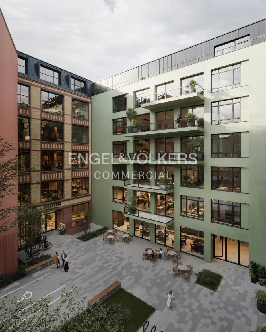 Courtyard view of modern buildings in peach and light green, with tables, benches, and people. "Engel & Volkers Commercial" logo overlay.