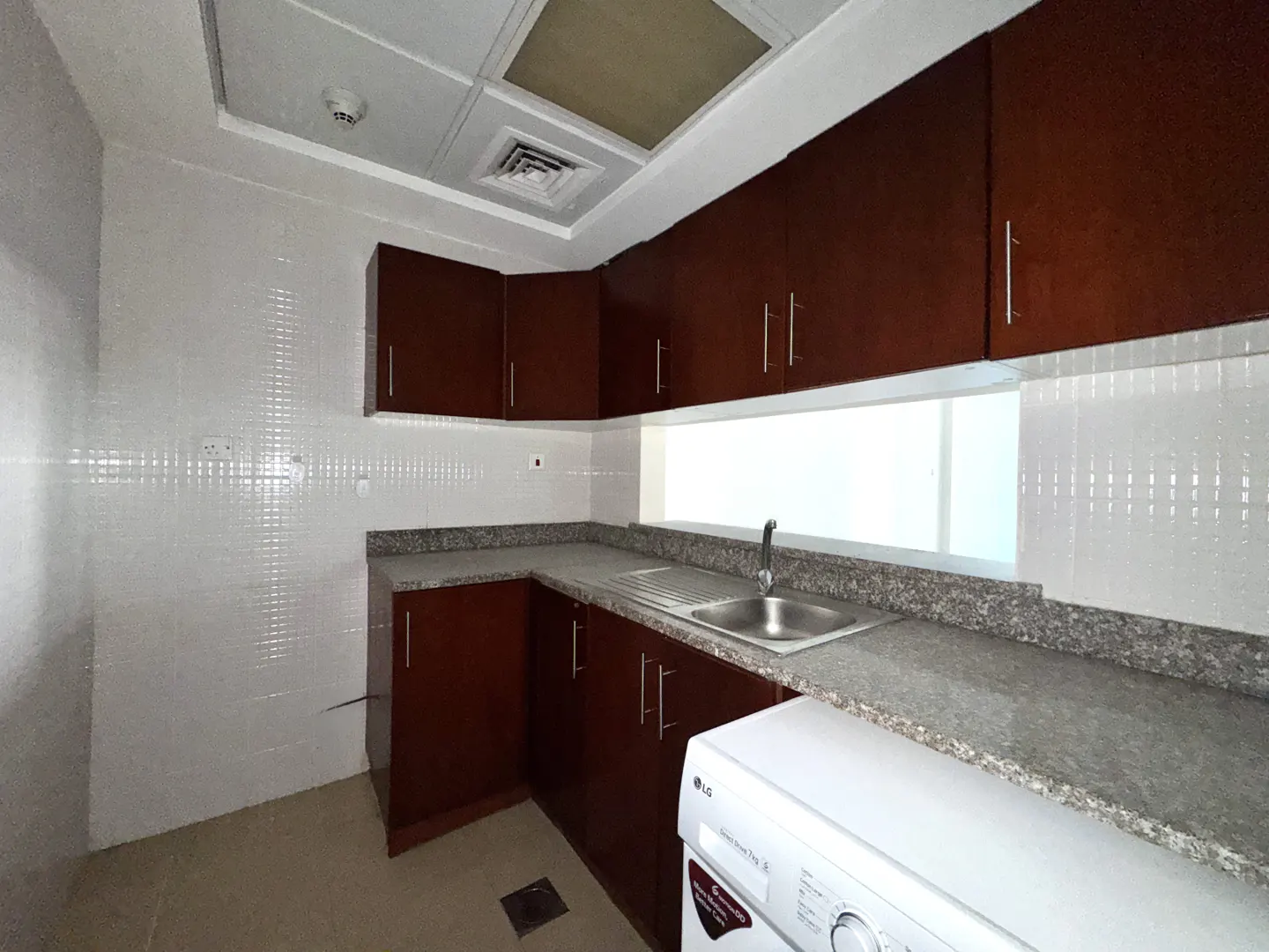 A kitchen with brown cabinets, gray countertops, white tiled walls, and a white washing machine.