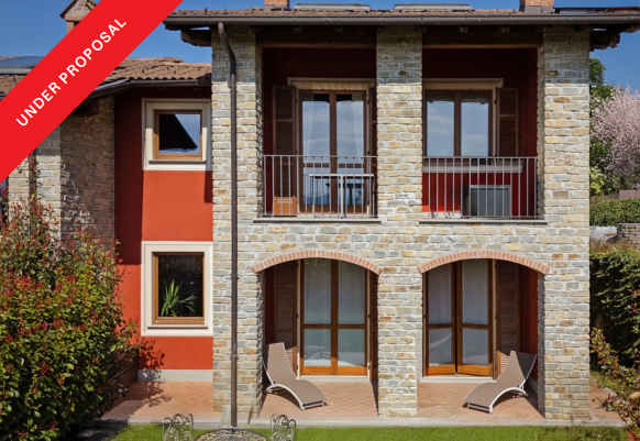 Two-story stone and red stucco house with a balcony, patio, lounge chairs, and an "Under Proposal" banner.
