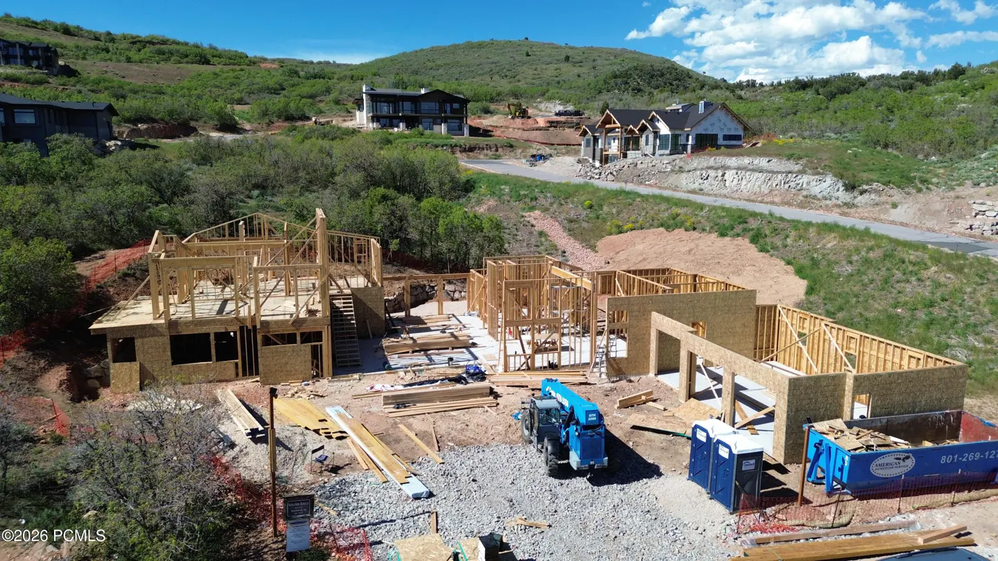 Aerial view of a wooden house frame under construction on a hillside with a blue crane and portable toilets on site.