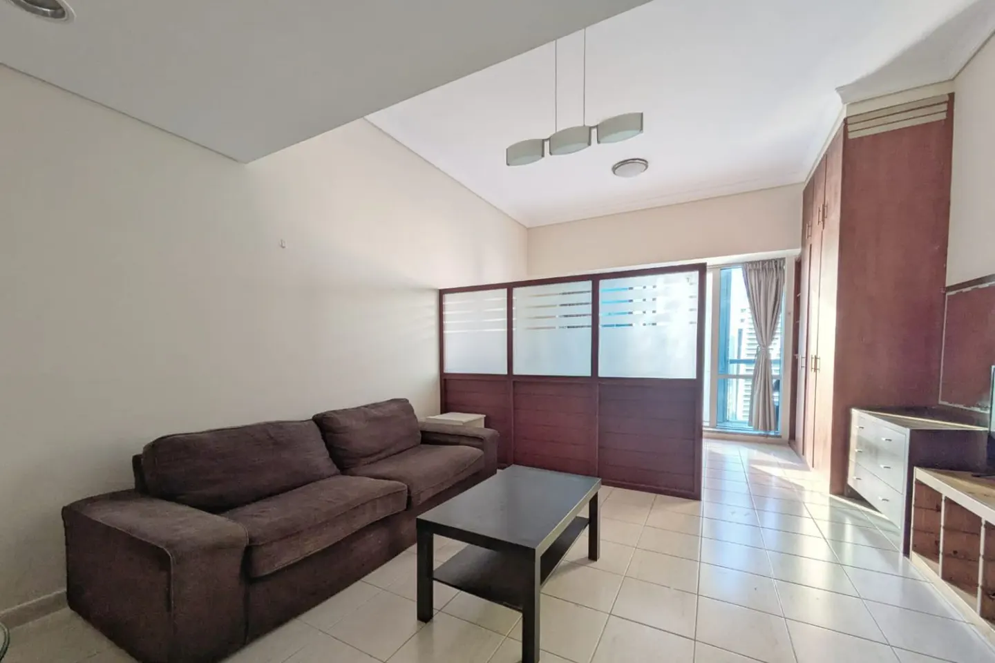 Living room with a brown sofa, black coffee table, and a wooden room divider separating the space from a windowed area.