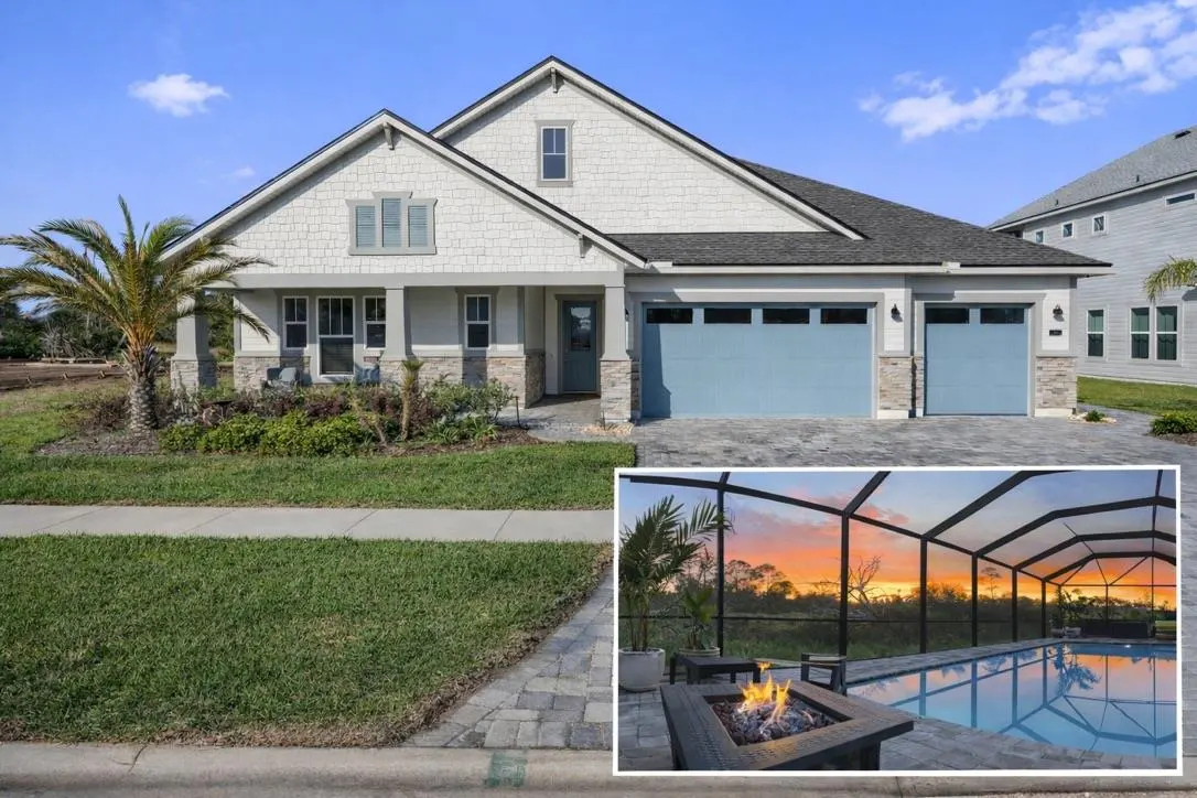 A light gray house with blue garage doors and a screened-in pool with a fire pit at sunset.