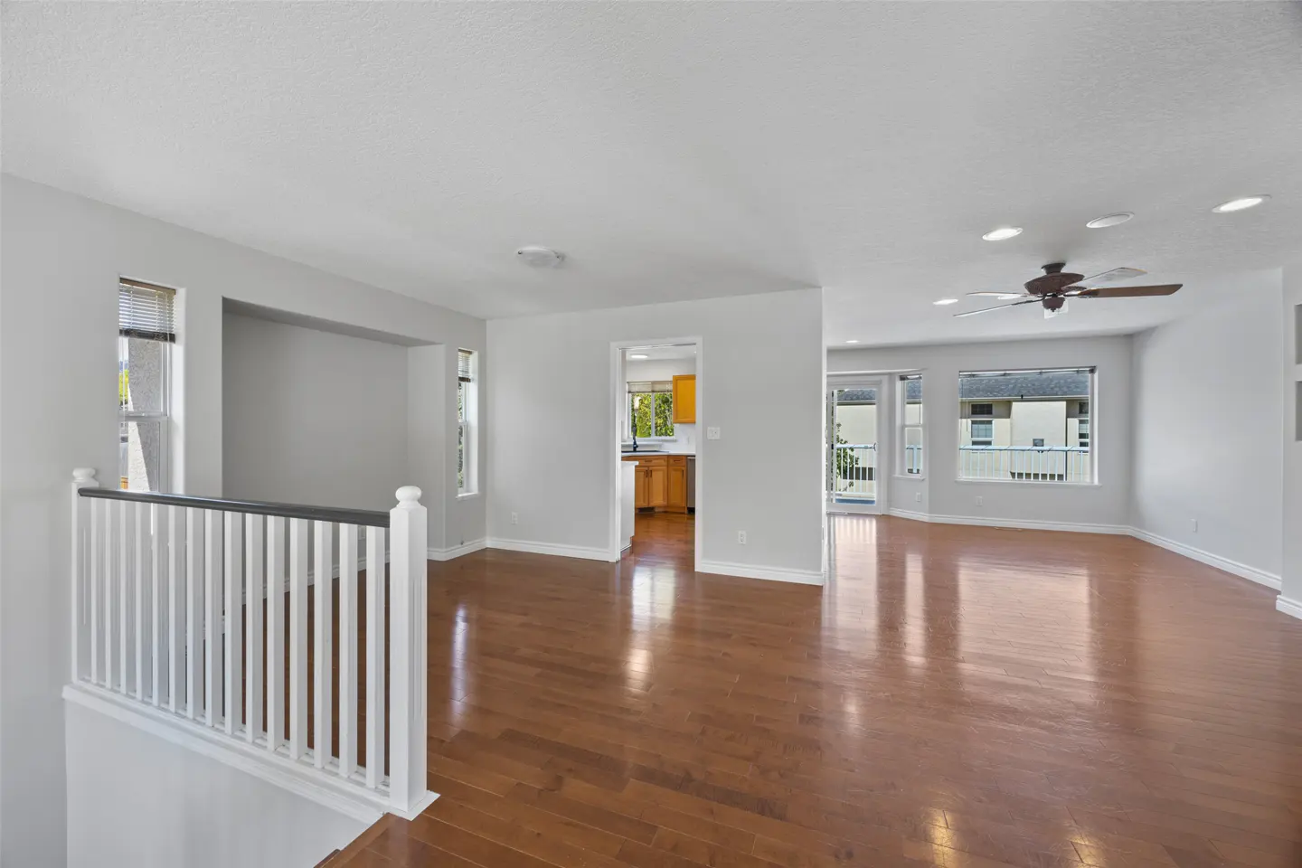 Bright, open-concept home with hardwood floors, white walls, and a ceiling fan. A glimpse of the kitchen is visible through an archway.