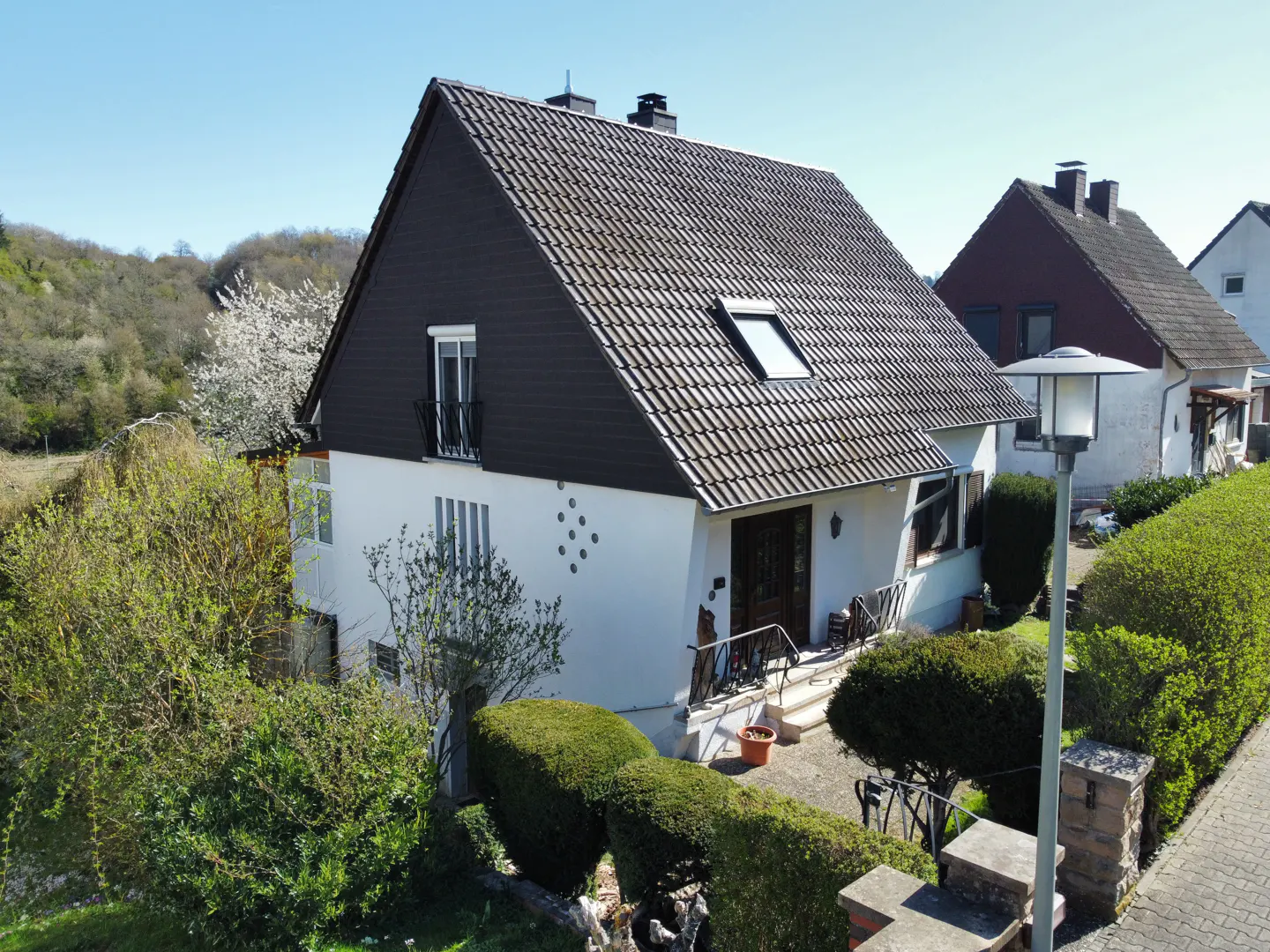 Two-story white house with a dark brown roof and green bushes in the front yard on a sunny day.