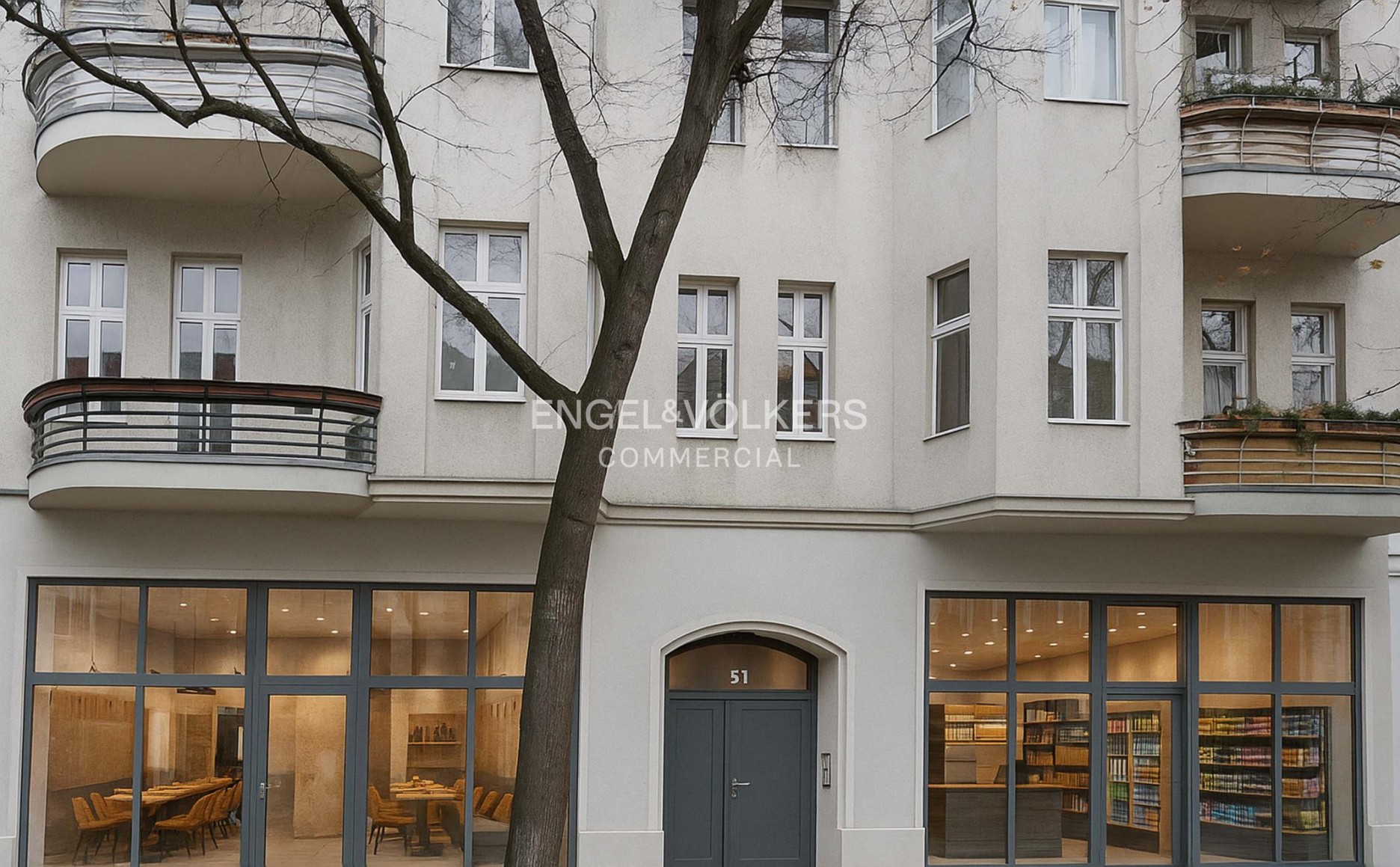 Exterior of a cream-colored building with balconies, a central entrance, and ground-floor retail spaces with large windows. [AI-generated text]
