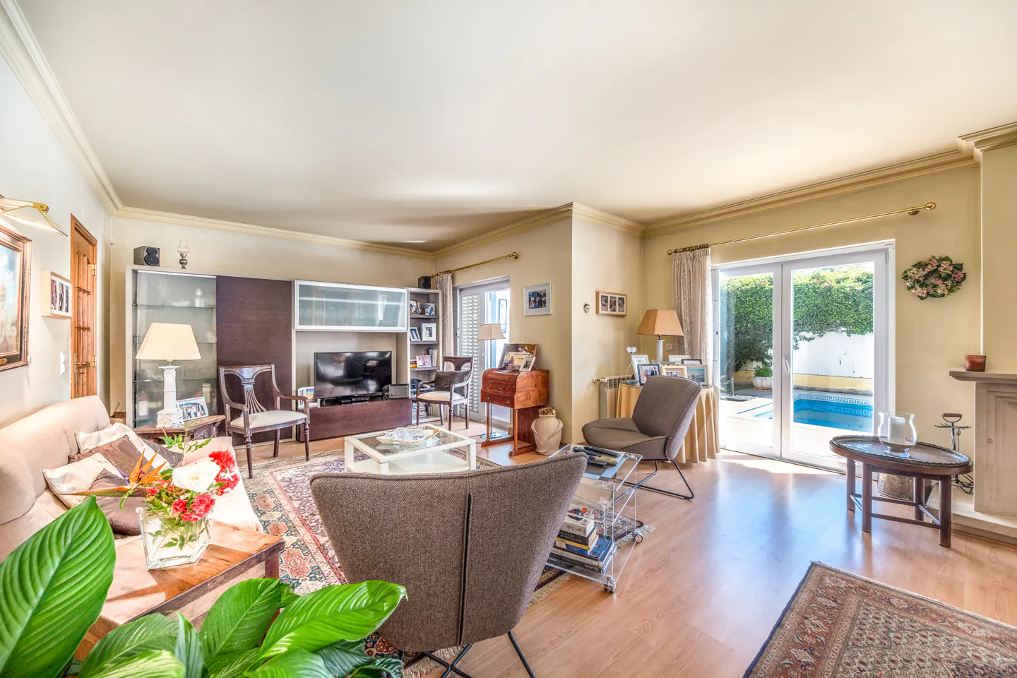 A living room with a sofa, chairs, TV, and sliding glass doors to a pool. The walls are light yellow.