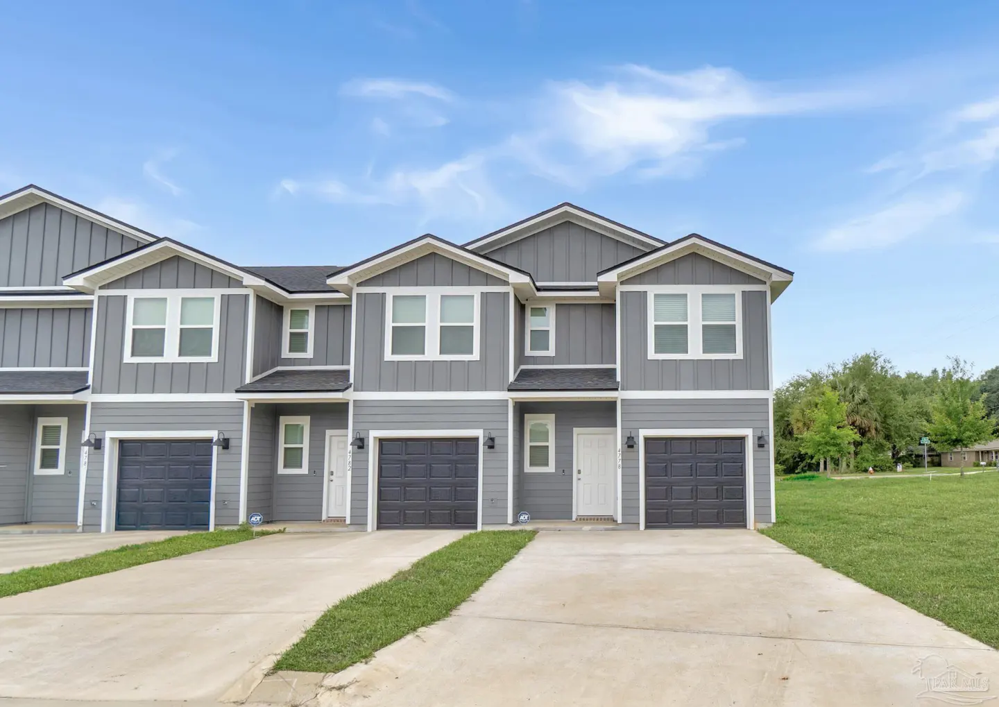 Three gray townhouses with black garage doors and white trim under a blue sky.