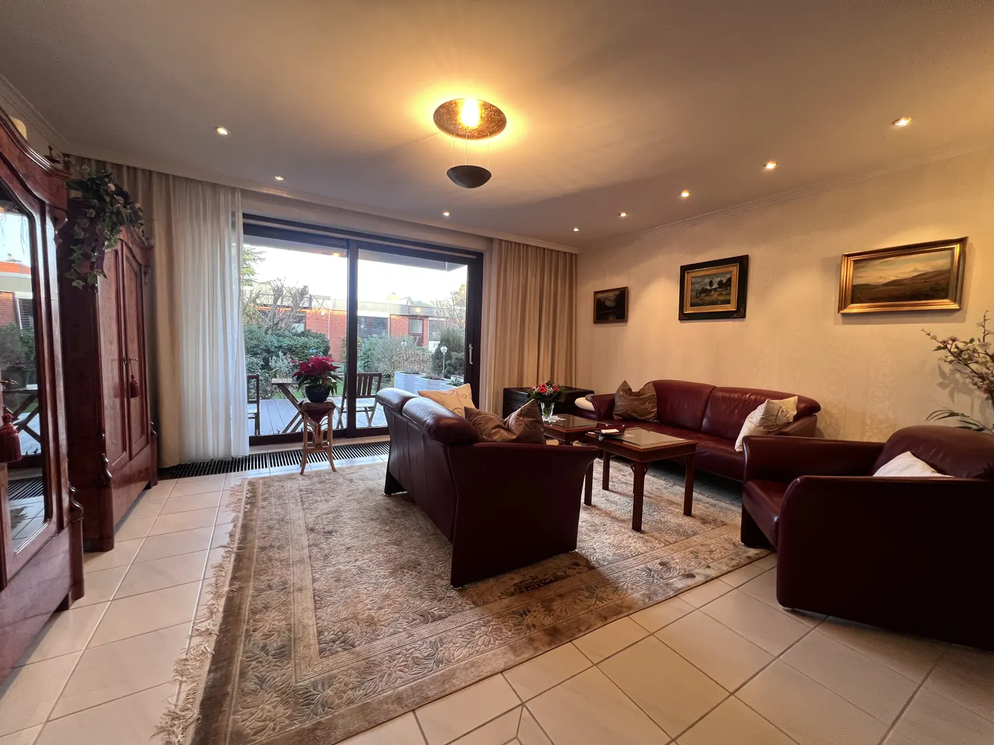 A living room with a brown leather sofa, chair, and a wooden coffee table on a patterned rug. A large sliding glass door leads to a patio.