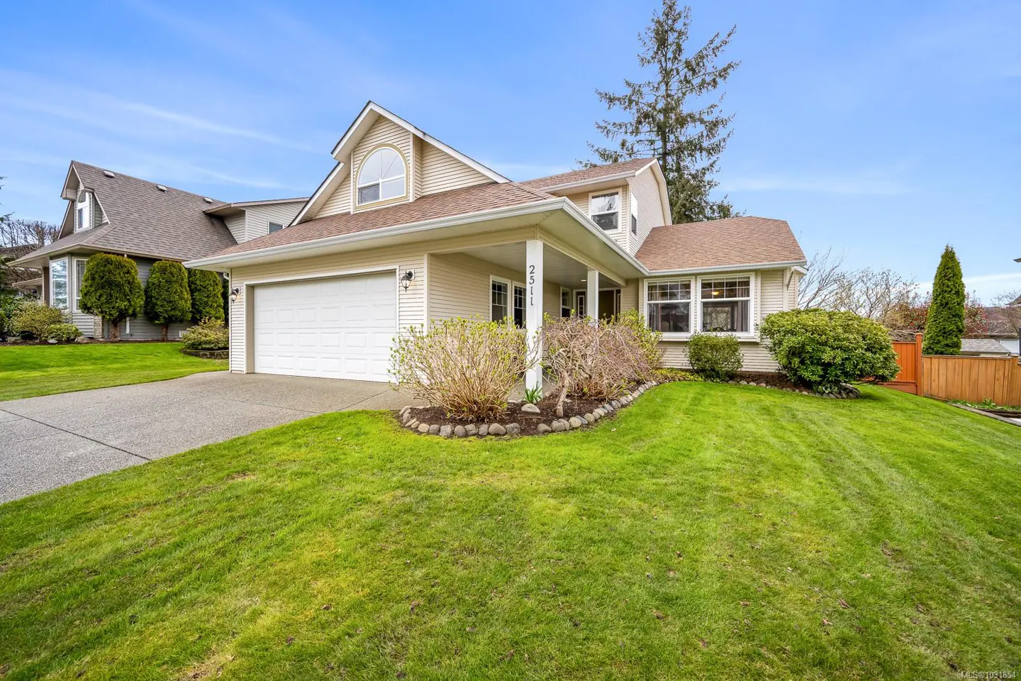 Beige two-story house with a white garage door, green lawn, and blue sky.