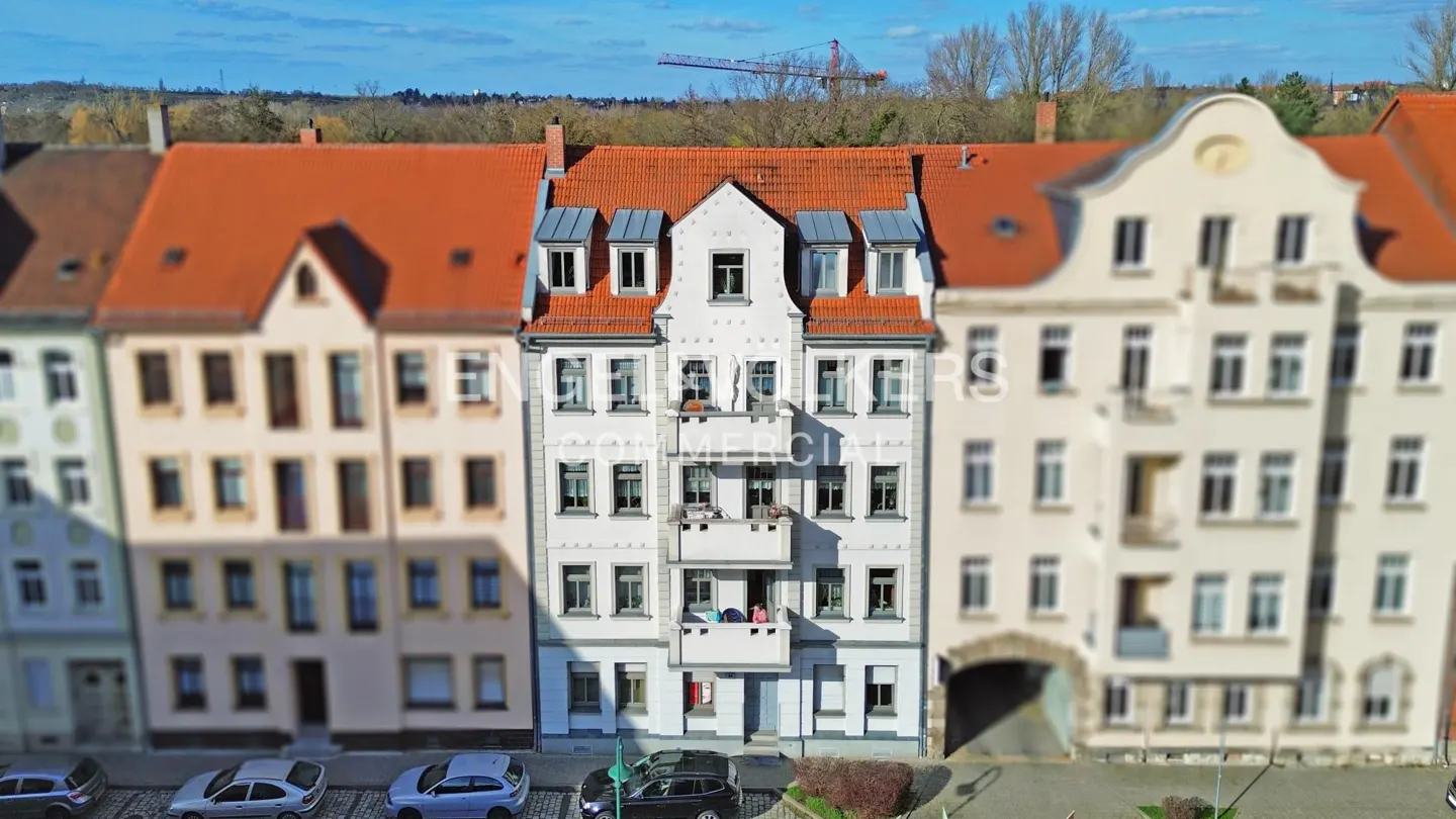 Row of European-style buildings with red tile roofs and parked cars on a sunny day.