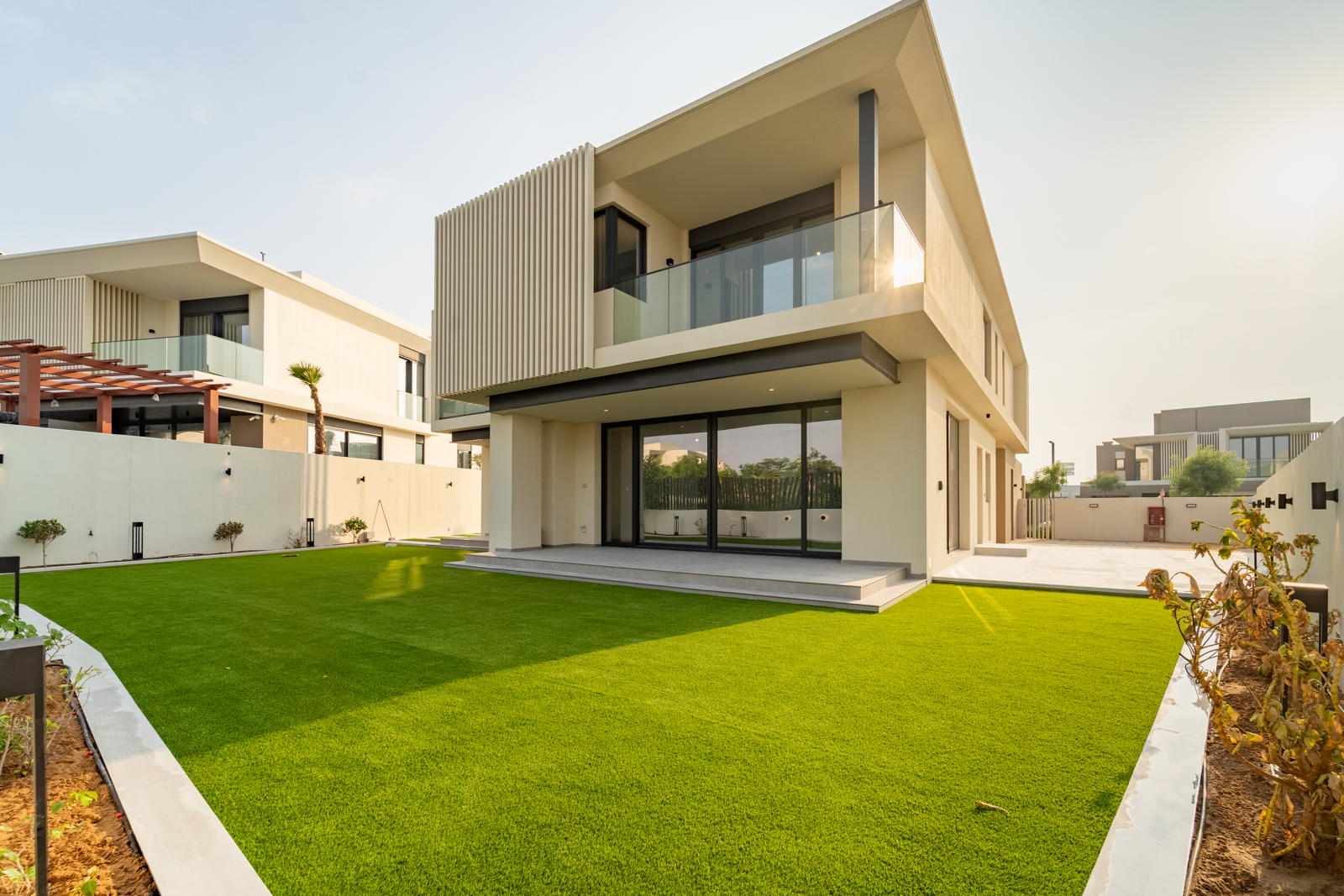 Modern two-story villa with a glass balcony, large sliding doors, and a well-maintained green lawn in a sunny backyard. [AI-generated text]