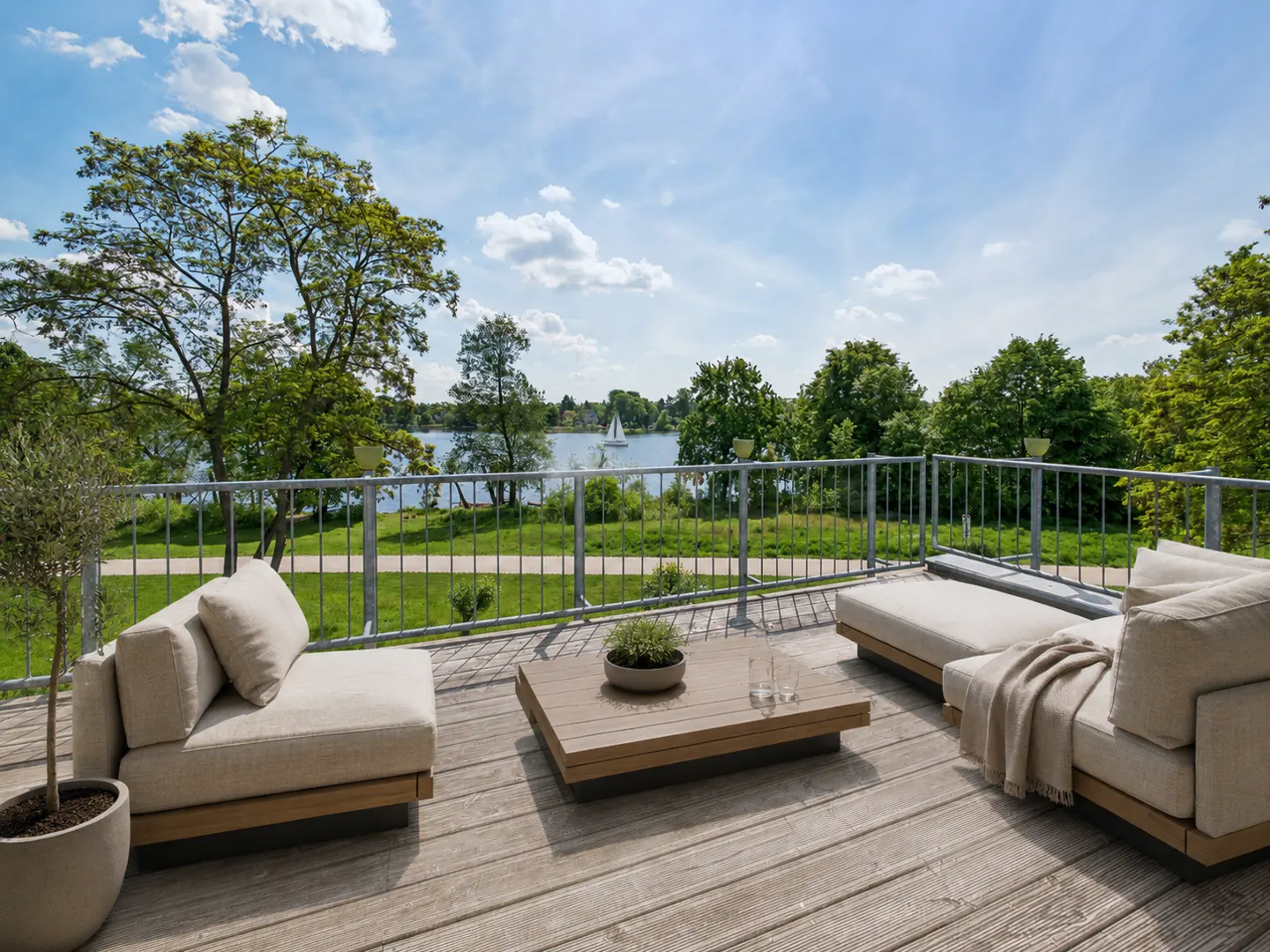 Outdoor patio with beige furniture, a wooden table, and a view of a lake with a sailboat.