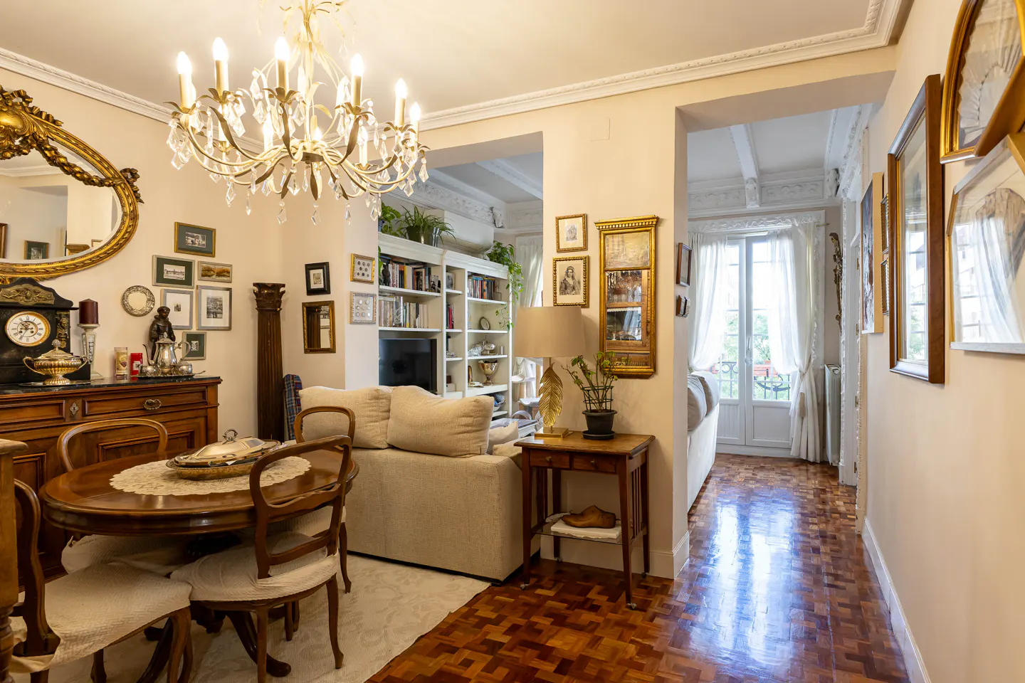 A living room with a dining table, sofa, bookshelf, and hallway with a balcony in the background.