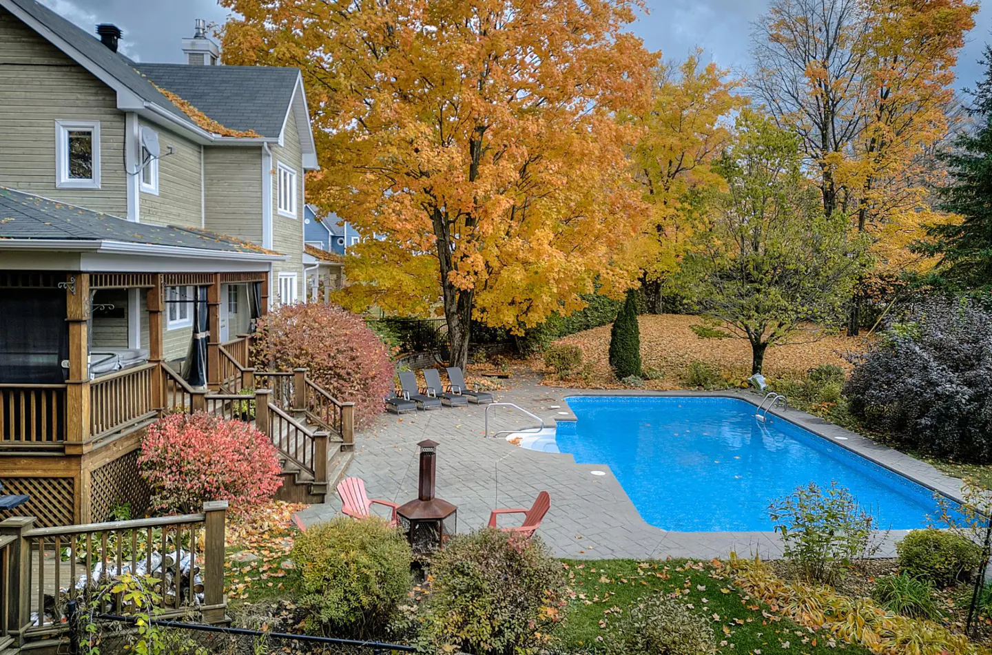 Backyard view of a two-story house with a pool, patio, and fall foliage.