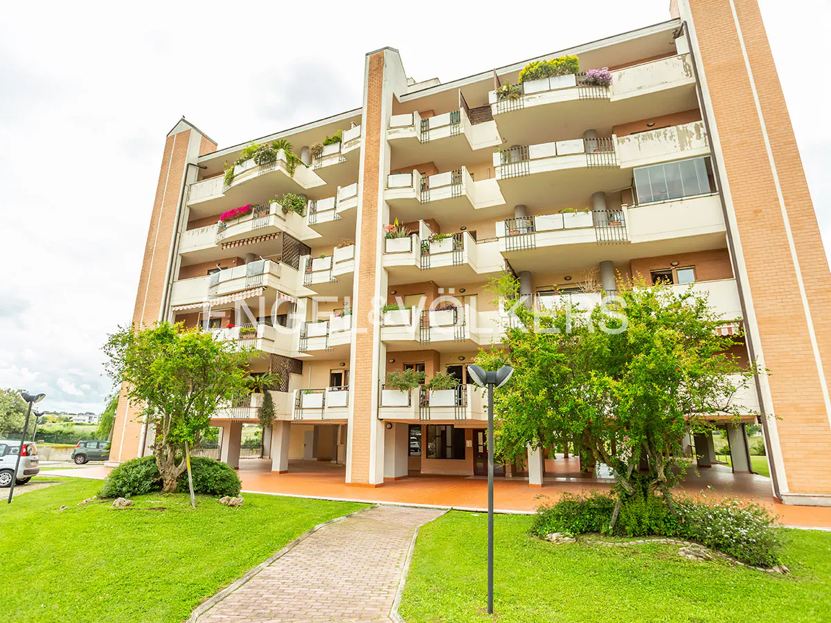 Exterior view of a multi-story apartment building with balconies, brick accents, and green lawn.