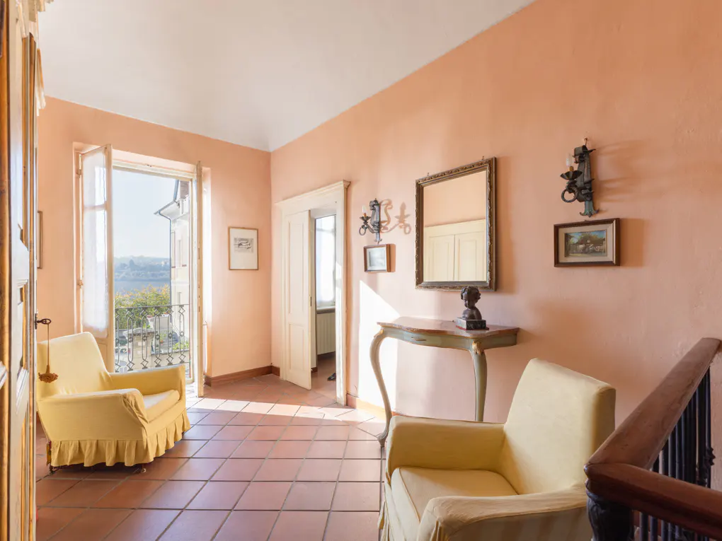 A room with peach walls, terracotta tile floor, yellow armchairs, and an open balcony door. A console table with a mirror and art adorns the wall.