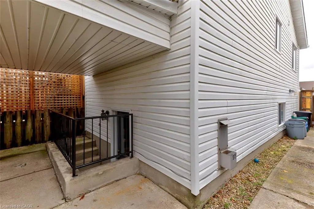 Exterior view of a white house with a basement entrance, black railing, and lattice fence.