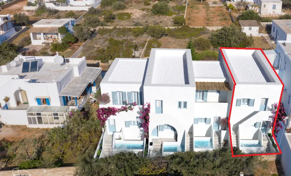 Aerial view of a white building with blue accents and a red outline, surrounded by greenery.